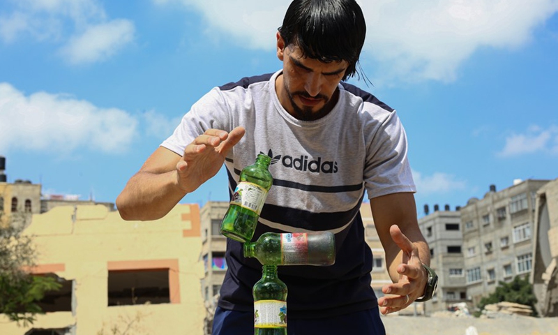 Palestinian balance artist Mohammed al-Shinbari practices balance art by using three empty class bottles, in the northern Gaza Strip town of Beit Hanoun, July 10, 2021.(Photo: Xinhua)
