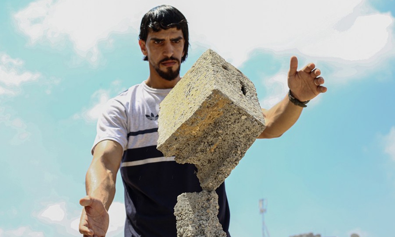 Palestinian balance artist Mohammed al-Shinbari lets a piece of concrete block from the rubble of war destruction stand on another, in the northern Gaza Strip town of Beit Hanoun, July 10, 2021.(Photo: Xinhua)