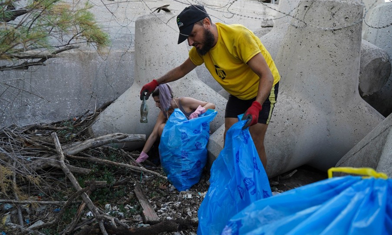 Η φωτογραφία που τραβήχτηκε στις 4 Ιουλίου 2021, δείχνει εθελοντές να συλλέγουν σκουπίδια μεταξύ σκυροδέματος τετραπόδων στην ακτή κοντά στον Πειραιά.  (Φωτογραφία: Xinhua)