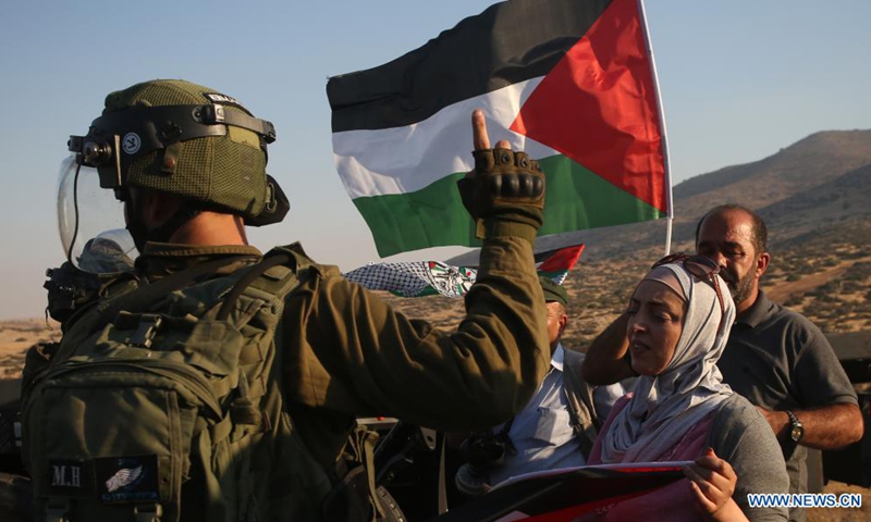 Protesters hold Palestinian flags in front of Israeli soldiers during a protest against the expanding of Jewish settlements at Tayasir checkpoint, east of the West Bank city of Tubas, July 31, 2021.(Photo: Xinhua)