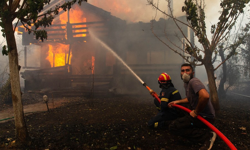 A firefighter and a volunteer try to put out a fire in Afidnes, some 30 kilometers away from the Greek capital of Athens, on Aug. 6, 2021.  (Photo: Xinhua)