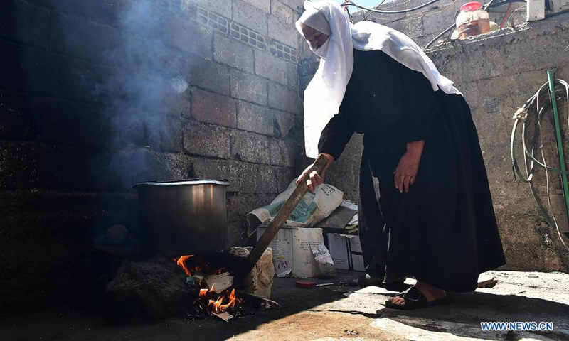 Nabiha Badour, a 75-year-old Syrian woman, lights up firewood in the backyard of her village house in the countryside of Sweida province, southern Syria, on June 21, 2021. Nabiha Badour refuses to stay home and wait for sons to take care of her. Instead, she chooses to do hard work to make her own living amid the harsh economic situation in the country.(Photo: Xinhua)