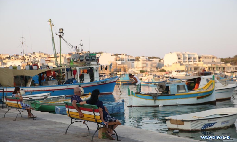 People spend time at dusk at a harbor in Marsaxlokk, a fishing village in Malta, on Aug. 14, 2021.(Photo: Xinhua)