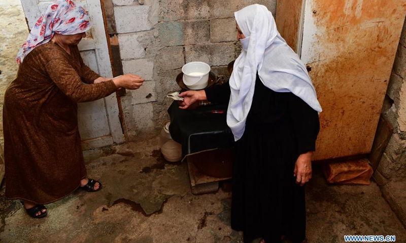 Nabiha Badour (R), a 75-year-old Syrian woman, sells milk in the backyard of her village house in the countryside of Sweida province, southern Syria, on June 21, 2021. Nabiha Badour refuses to stay home and wait for sons to take care of her. Instead, she chooses to do hard work to make her own living amid the harsh economic situation in the country.(Photo: Xinhua)