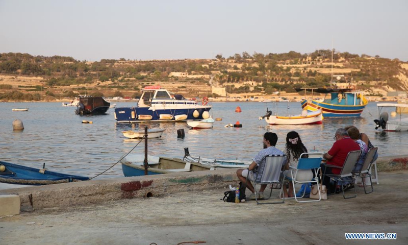 People spend time at dusk at a harbor in Marsaxlokk, a fishing village in Malta, on Aug. 14, 2021.(Photo: Xinhua)
