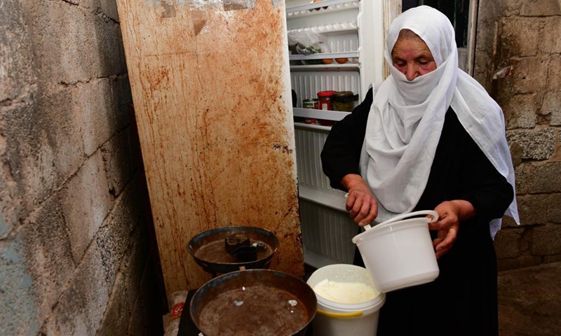 Nabiha Badour, a 75-year-old Syrian woman, prepares dairy food in the backyard of her village house in the countryside of Sweida province, southern Syria, on June 21, 2021. Nabiha Badour refuses to stay home and wait for sons to take care of her. Instead, she chooses to do hard work to make her own living amid the harsh economic situation in the country.(Photo: Xinhua)