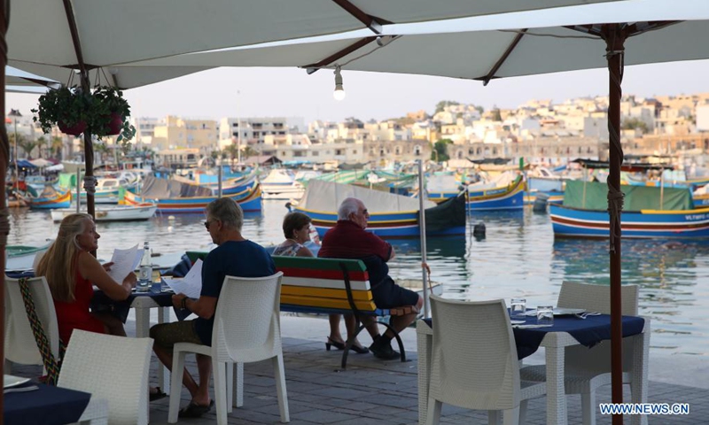 People spend time at dusk at a harbor in Marsaxlokk, a fishing village in Malta, on Aug. 14, 2021.(Photo: Xinhua)