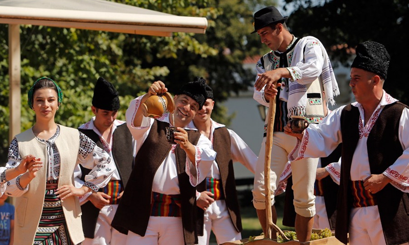 Men dressed in traditional clothes perform a demonstration of ancient wine making at an autumn fair at Romanian Village Museum in Bucharest, Romania, Sept. 11, 2021.(Photo: Xinhua)