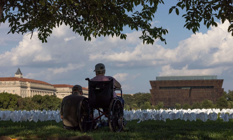 Visitors sit beside white flags placed on the National Mall to honor the lives lost to COVID-19 in Washington, D.C., the United States, Sept. 18, 2021.(Photo: Xinhua)