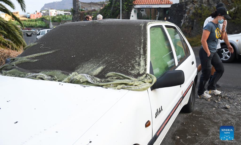 People walk past a vehicle covered by volcanic ash on the island of La Palma in the Canary Islands, Spain, on Sept. 22, 2021. The eruption of the Cumbre Vieja volcano is expected to last between 24 and 84 days, the Volcanology Institute of the Canary Islands (INVOLCAN) said on Wednesday.(Photo: Xinhua)