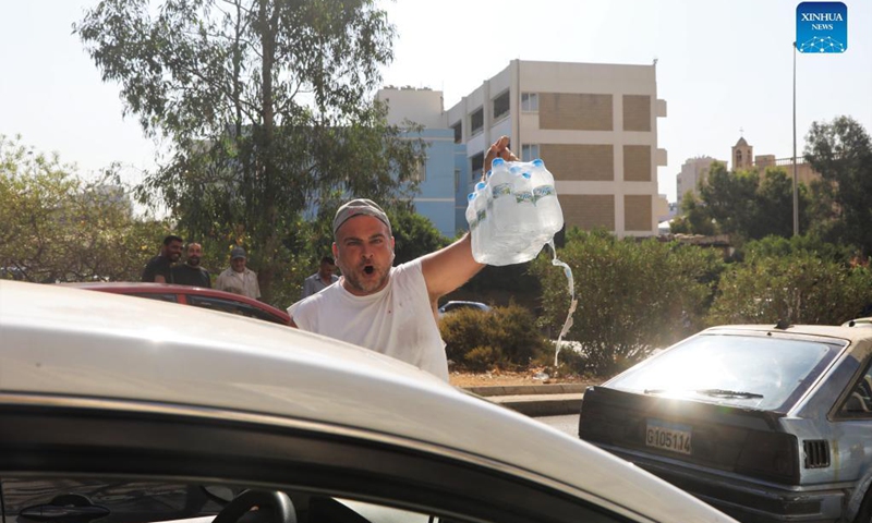 A peddler of bottled water is seen among cars waiting for fuel on a main road near a gas station in Beirut, Lebanon, on Sept. 21, 2021. Lebanon's Energy Ministry has raised gasoline prices for the second time in less than a week, effectively ending its fuel subsidy.(Photo: Xinhua)
