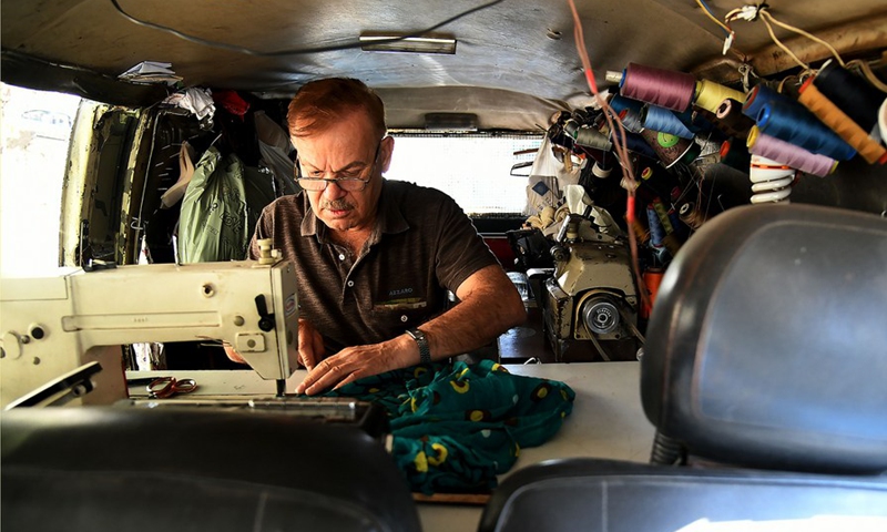 Jamal al-Masri fixes clothes for a passersby inside his old van in Damascus, capital of Syria, on Oct. 4, 2021.(Photo: Xinhua)