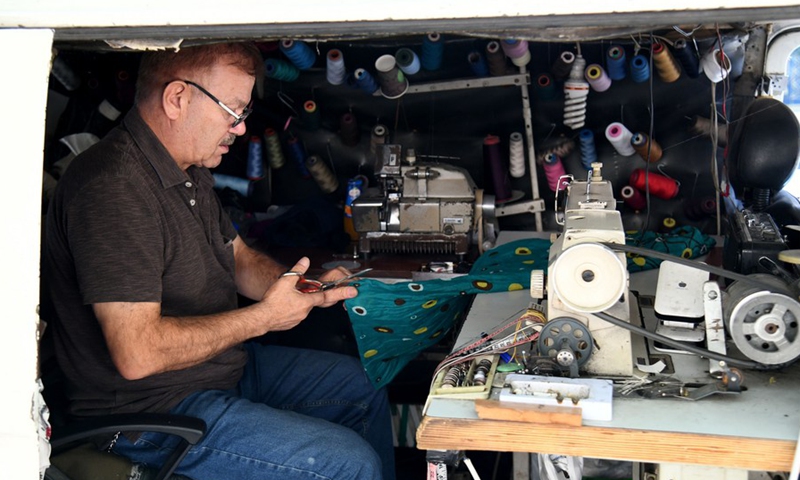 Jamal al-Masri fixes clothes for a passersby inside his old van in Damascus, capital of Syria, on Oct. 4, 2021.(Photo: Xinhua)