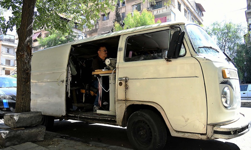 The 65-year-old tailor Jamal al-Masri fixes clothes to passersby inside his old van in Syrian capital Damascus on Oct. 4, 2021. (Photo: Xinhua)