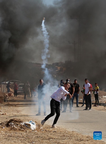 A Palestinian protester throws back a tear gas canister fired by Israeli soldiers during a protest against the expansion of Jewish settlements in the West Bank village of Beit Dajan, east of Nablus, on Oct. 22, 2021.(Photo: Xinhua)