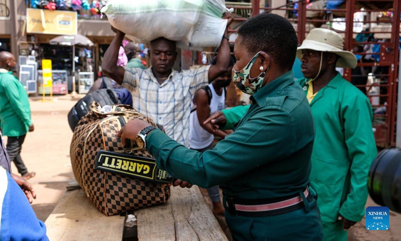 A bus security officer (front) checks luggage of a passenger at a bus terminal in Kampala, Uganda, on Oct. 26, 2021. Police on Tuesday morning spent several hours at the bus terminals in the capital Kampala, urging people to be vigilant and report any suspicious characters. Bus operators were also instructed to resume security checks of all passengers boarding.(Photo: Xinhua)