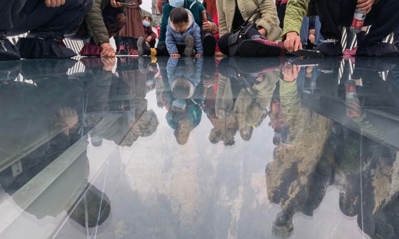 Tourists look through a glass-bottomed bridge at Zhangjiajie Grand Canyon, central China's Hunan Province, on Nov. 12, 2021. The 430-meter long, six-meter wide bridge, linking two steep cliffs 300 meters above the ground, is paved with 99 panes of three-layer transparent glass.Photo:Xinhua