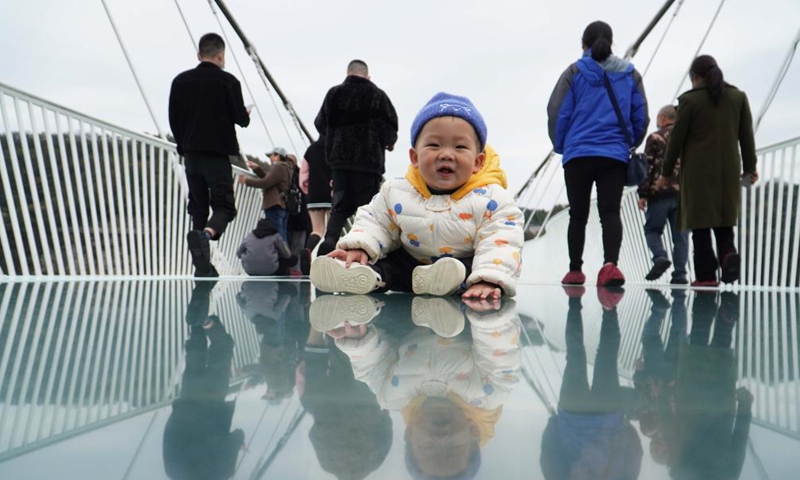 A baby sits on a glass-bottomed bridge at Zhangjiajie Grand Canyon, central China's Hunan Province, on Nov. 12, 2021. The 430-meter long, six-meter wide bridge, linking two steep cliffs 300 meters above the ground, is paved with 99 panes of three-layer transparent glass.Photo:Xinhua