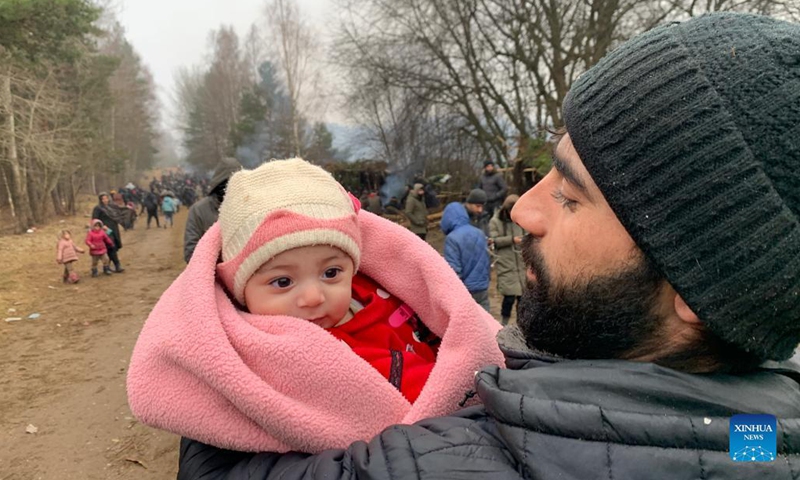 A refugee carries an infant at a refugee camp near the Belarusian-Polish border in Belarus, Nov. 14, 2021. Belarusian President Alexander Lukashenko ordered on Nov. 13 to set up tents and distribute relief supplies to refugees gathered near the Belarusian-Polish border.(Photo: Xinhua)