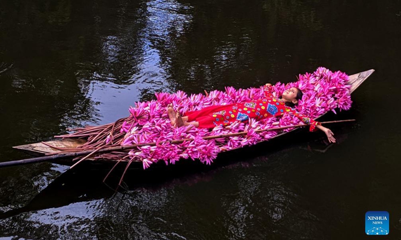 A girl poses for a photo while lying on a boat loaded with red water lilies in Barisal, Bangladesh, Nov. 16, 2021. 