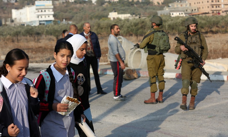Palestinian students walk to their school while Israeli soldiers stand guard in the village of al-Lubban ash-Sharqiya near the West Bank city of Nablus, on Nov. 18, 2021.(Photo: Xinhua)