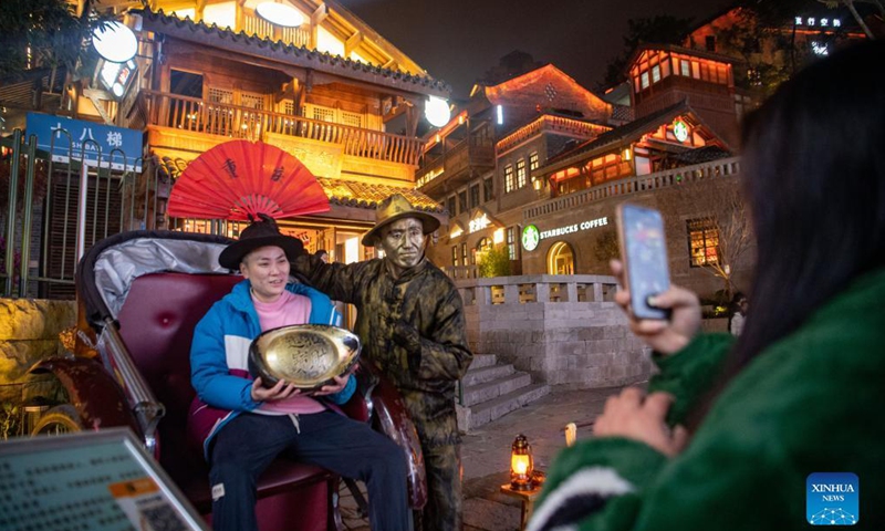 A tourist poses for photos with an actor who desses up as a bronze statue in southwest China's Chongqing Municipality, Dec. 9, 2021. Chongqing has adopted various activities to promote night economy.Photo:Xinhua