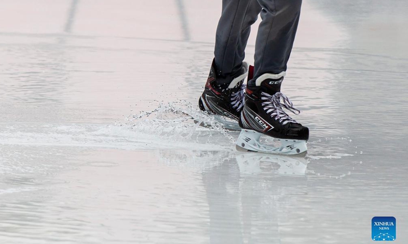 a man skates on an outdoor ice rink during an unusually warm day