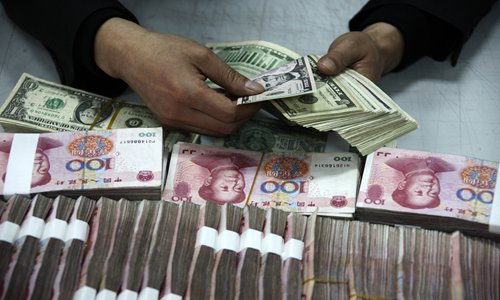 A Chinese clerk counts US dollar banknotes next to yuan bills at a bank in Huaibei, East China's Anhui province. File photo: IC