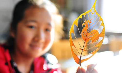 A student shows the leaf carving work Rooster of Liu Ping, an art teacher of Qingdao Experimental Primary School, east China's Shandong Province, Jan. 11, 2017. Liu loves this type of art and spends her spare time on creating various works inspired by traditional papercutting. (Xinhua/Wang Haibin) 

