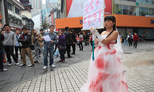 A performance artist wears a wedding dress splattered with red spots and holds a board that reads “Anti-domestic violence, no harm”at a street in Shenzhen, South China’s Guangdong Province, on December 10, 2014. Photo: CFP