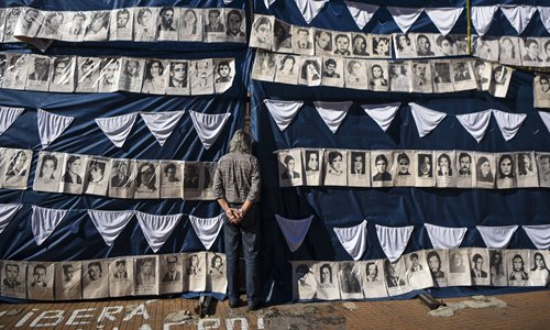 A man peers behind portraits of victims of forced disappearance in the Plaza de Mayo square in Buenos Aires, Argentina, on Saturday, during events held to commemorate the 40th anniversary of the first protest around the square by the Argentine human rights group 