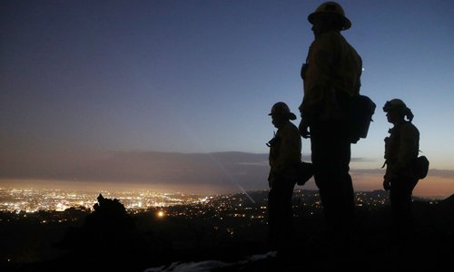Firefighters stand while monitoring Griffith Park, with the lights of the city below, in the aftermath of a fire in the park on Tuesday in Los Angeles, California. Tourists had to be evacuated from the 25-acre brush fire in the park. Numerous fires have sparked in Southern California from an ongoing heat wave. Photo: AFP