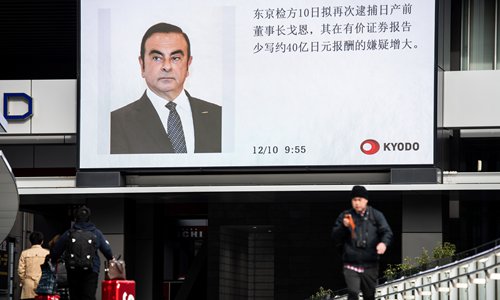 Pedestrians walk past a television screen showing a news report on former Nissan chief Carlos Ghosn, who is charged with financial misconduct, in Tokyo, Japan on Monday. Photo: AFP  