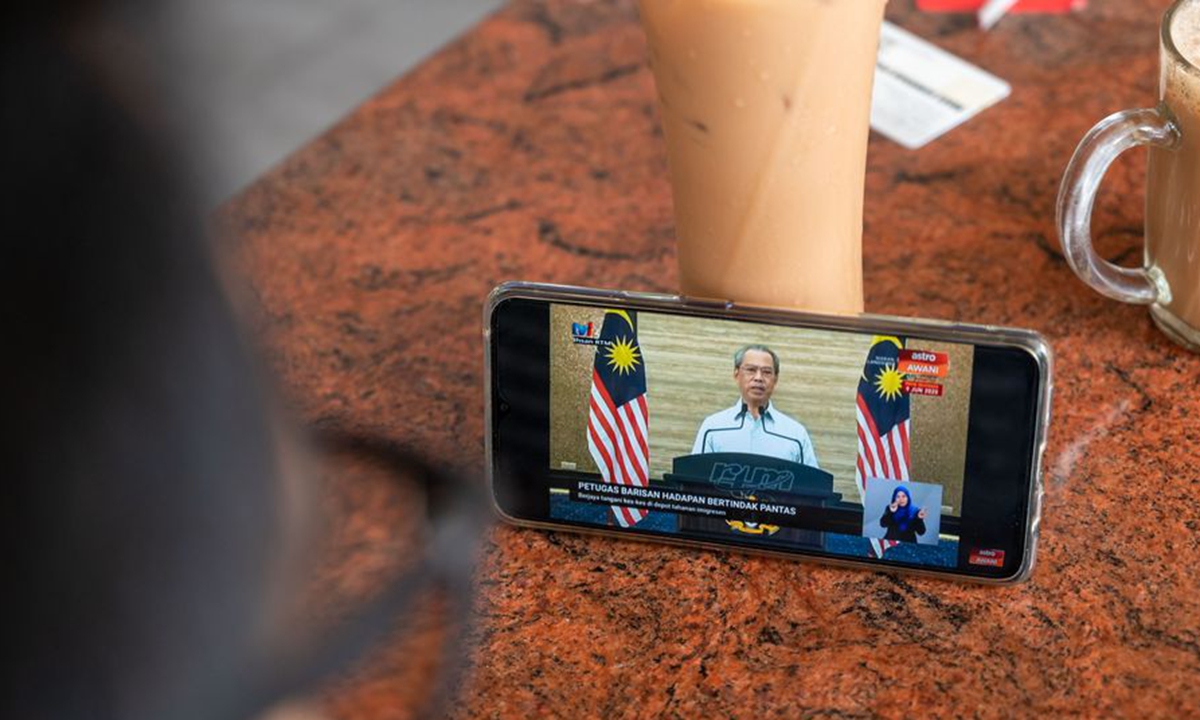 A customer watches a televised speech by Malaysian Prime Minister Muhyiddin Yassin via mobile phone in Kuala Lumpur, Malaysia, June 7, 2020. (Xinhua/Zhu Wei)