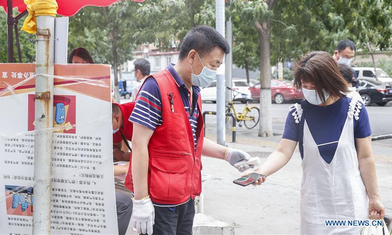 A community staff member checks a resident's body temperature at the entrance of a community in Xicheng District of Beijing, capital of China, June 17, 2020. Beijing has upgraded its emergency response to COVID-19 from Level III to Level II, the second-highest of the four-tier system, as the city is battling to contain new clusters of COVID-19. Following the upgrade of emergency response, closed-off management has been resumed in all communities in Beijing and those who seek to enter are required to go through four steps -- having their body temperature tested, showing a registered pass, having their health code checked and completing real-name registration, together with strict exit controls. (Xinhua/Zhang Yuwei) 