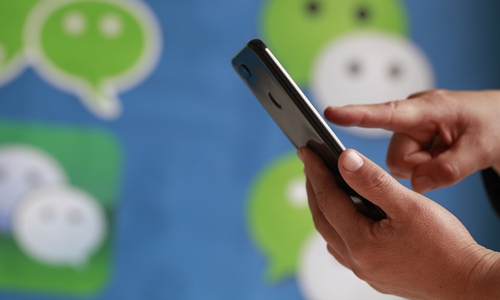 A user swipes on his smartphone while WeChat logos appear in the background, 14 May 2020. Photo: IC