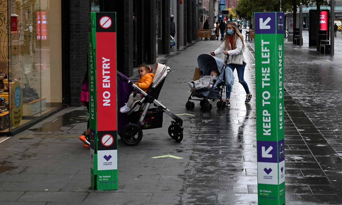 A pedestrian wearing a face mask or covering due to the COVID-19 pandemic, walks past barriers advertising a one-way system for shoppers, in Liverpool, north west England on October 13, 2020, as new local lockdown measures are set to be imposed to help stem a second wave of the novel coronavirus COVID-19. Photo: AFP