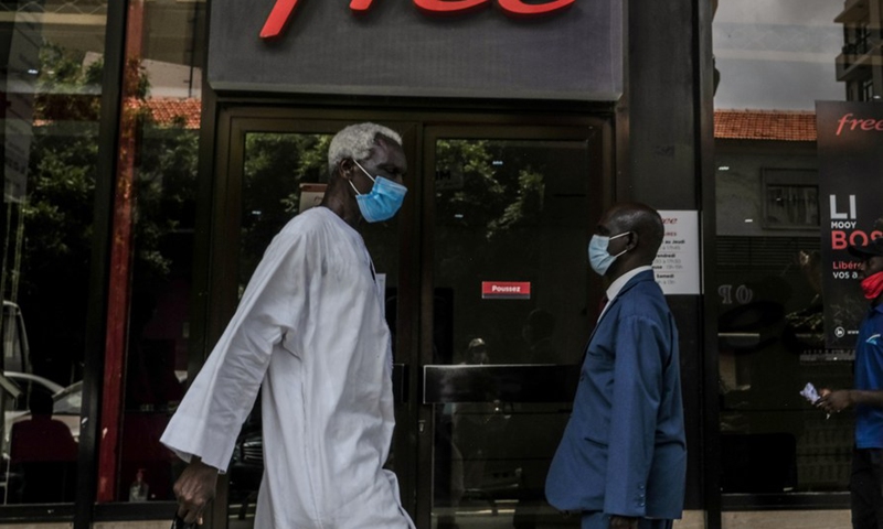 People wearing face masks walk past a store in central Dakar, Senegal, on July 21, 2020. (Photo by Eddy Peters/Xinhua)