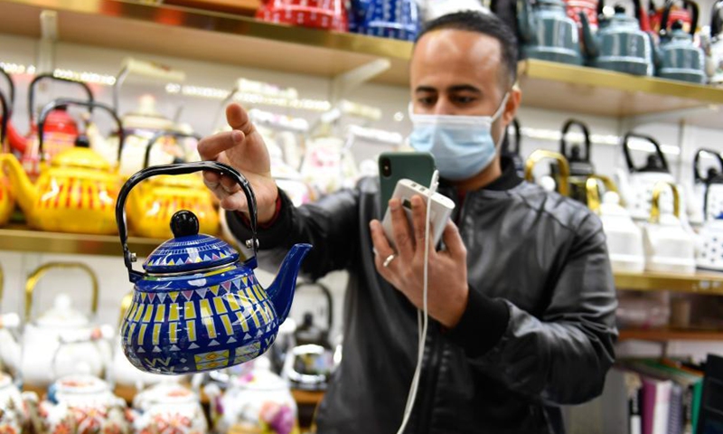 A Yemeni trader selects tea pots while communicating with his Saudi Arabian client via video link at the Yiwu International Trade Market in Yiwu City of east China's Zhejiang Province, Jan. 14, 2021. Facing the onslaught of COVID-19 pandemic, authorities in Yiwu City, dubbed 