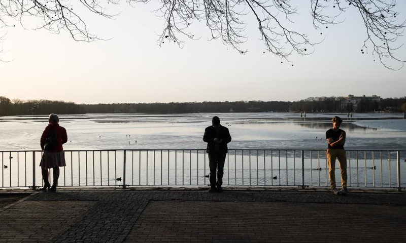Three visitors enjoy sunshine by the Lake Tegel covered with thin ice in Berlin, capital of Germany, Feb. 25, 2021. (Xinhua/Shan Yuqi)  