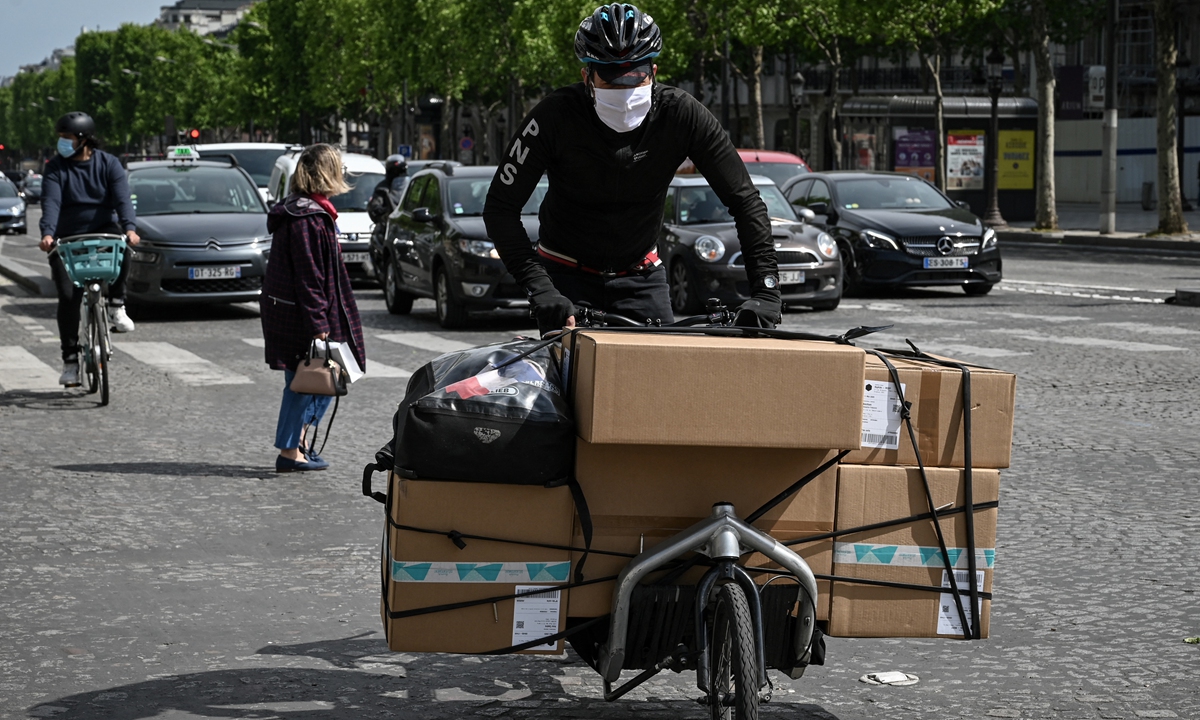 A delivery rider carries packages on a bicycle along The Champs Elysees Avenue in Paris on May 11, 2020. 
Right: A rider working for the food delivery company Deliveroo piles up his delivery bag in front of the company's offices in Bordeaux, southwestern France, on August 28, 2017. Photos: AFP