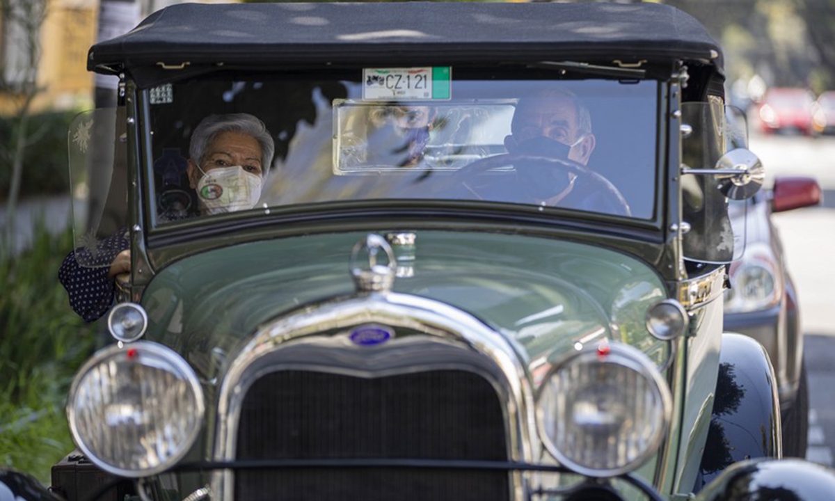 People wearing face masks drive a vintage car in Mexico City, Mexico, on Oct. 25, 2020. (Photo by Ricardo Flores/Xinhua)