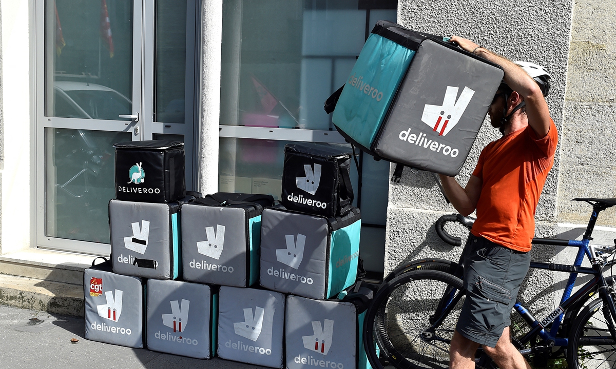 A delivery rider carries packages on a bicycle along The Champs Elysees Avenue in Paris on May 11, 2020. 
Right: A rider working for the food delivery company Deliveroo piles up his delivery bag in front of the company's offices in Bordeaux, southwestern France, on August 28, 2017. Photos: AFP