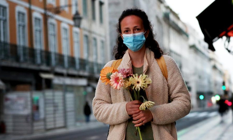 A woman wearing a protective face mask and holding flowers walks in downtown Lisbon, Portugal, on March 8, 2021, on occasion of the International Women's Day.Photo:Xinhua