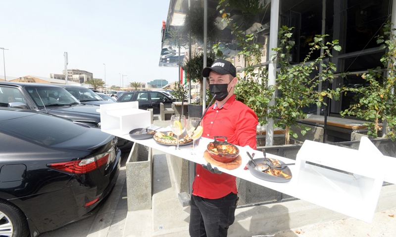 A waiter delivers meals to customers waiting inside their cars outside a restaurant in Kuwait City, Kuwait, on March 10, 2021. (Photo: Xinhua)