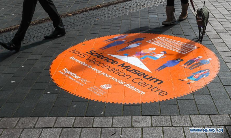 Photo taken on March 11, 2021 shows people walking past a sign on the road outside the NHS COVID-19 Vaccination Centre in the Science Museum in London, Britain.(Photo:Xinhua)