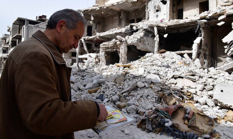 Hadi Ghusoun, a retired English teacher in his late 60s, looks at old certificates, which he had found under the rubble of his shattered house in Homs city in central Syria, March 11, 2021.(Photo: Xinhua)