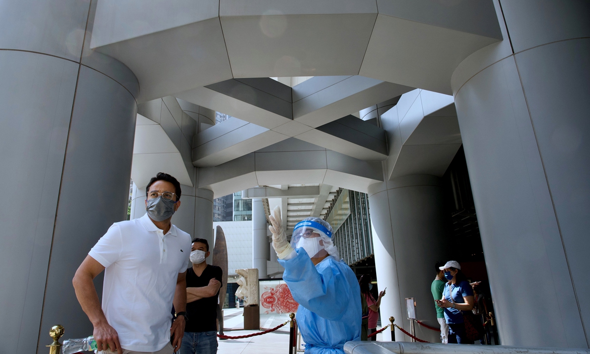 A staff member in a protective suit directs an HSBC employee to a temporary testing center for COVID-19 near the entrance to the bank's headquarters in Hong Kong on Wednesday. HSBC closed its Hong Kong headquarters after three coronavirus infections were confirmed. Photo: VCG