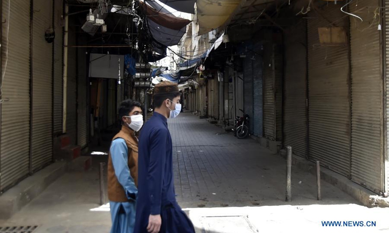 People wearing face masks walk past a closed market in northwest Pakistan's Peshawar on March 20, 2021. Pakistan is facing a serious third wave of the virus and the government is taking steps to ensure the standard operating procedures to control the spread of the virus.(Photo: Xinhua)
