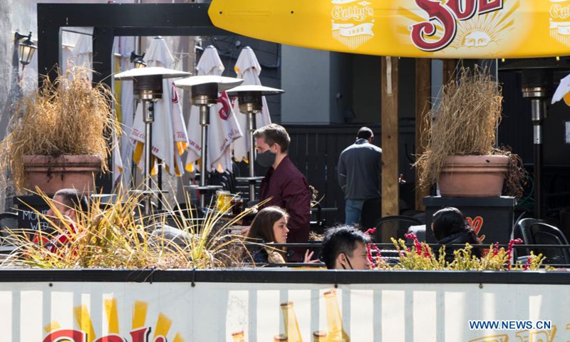 A waiter wearing a face mask serves customers at the outdoor area of a restaurant in Toronto, Canada, on March 20, 2021. With distancing rules and a number of other public health and workplace safety measures, outdoor dining was allowed to resume Saturday in Toronto under modifications to the Ontario's color-coded pandemic response framework. (Photo by Zou Zheng/Xinhua)

